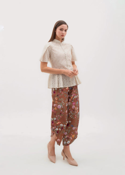A woman modeling a traditional-style outfit consisting of a short-sleeve cream lace top and brown floral wide-leg pants.